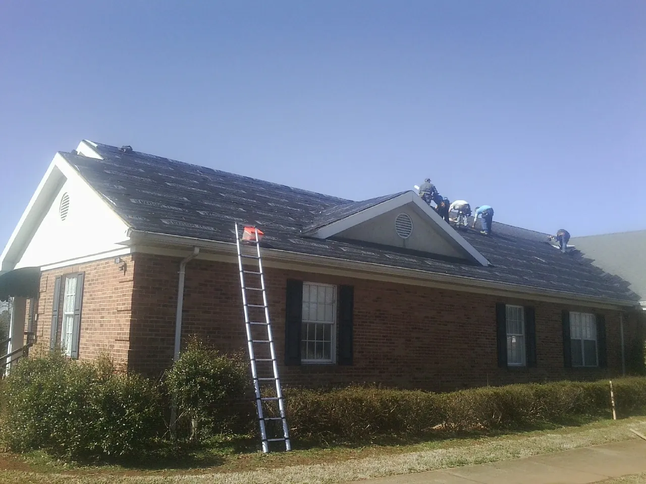 Crew tearing shingles off a brick ranch roof with a ladder set — Metal Roof Repair work by our crew in Gibbonsville