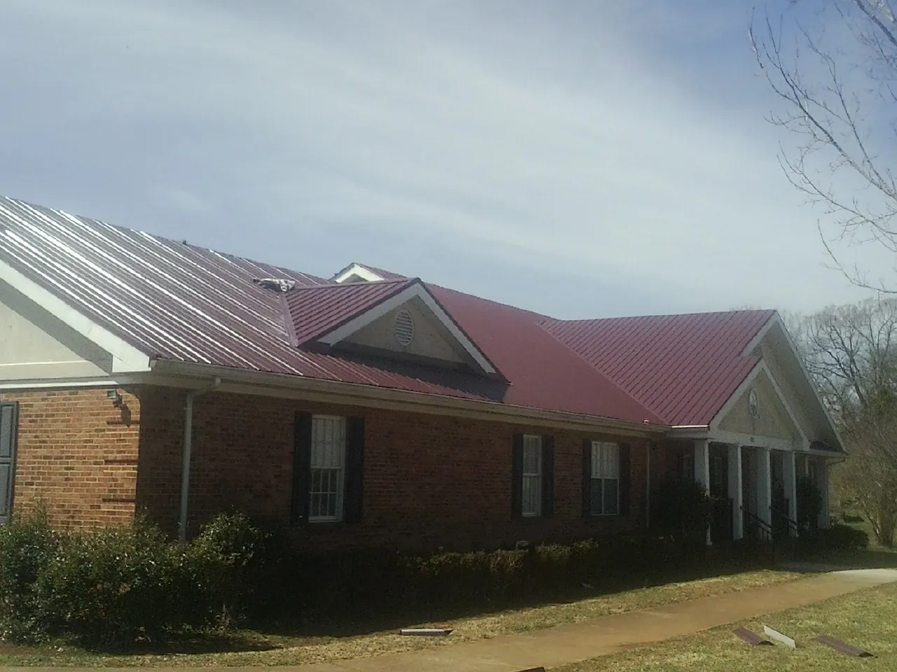 Red metal roof with gabled entries on a long brick building, from a Hail Damage Roof Repair job in Gibbonsville