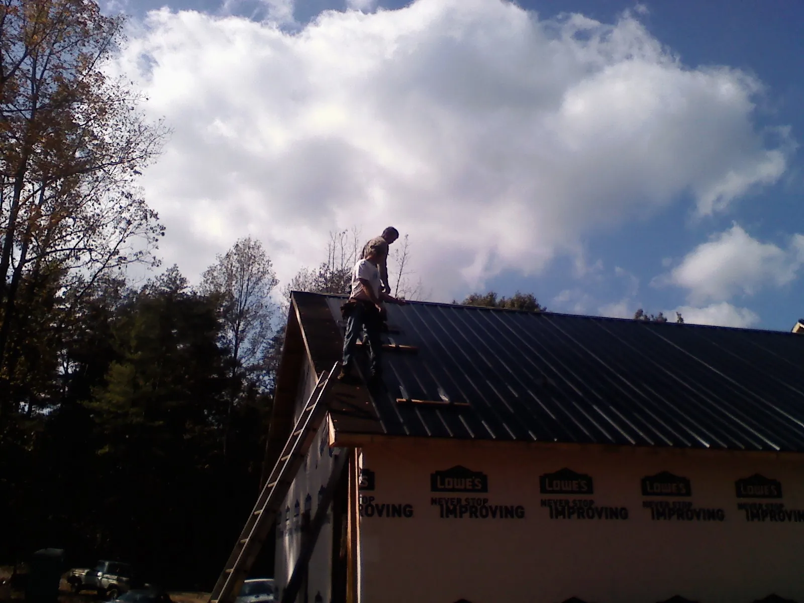 Roofer fastening dark metal panels high against a cloudy sky, from a Roof Inspection job in Gibbonsville
