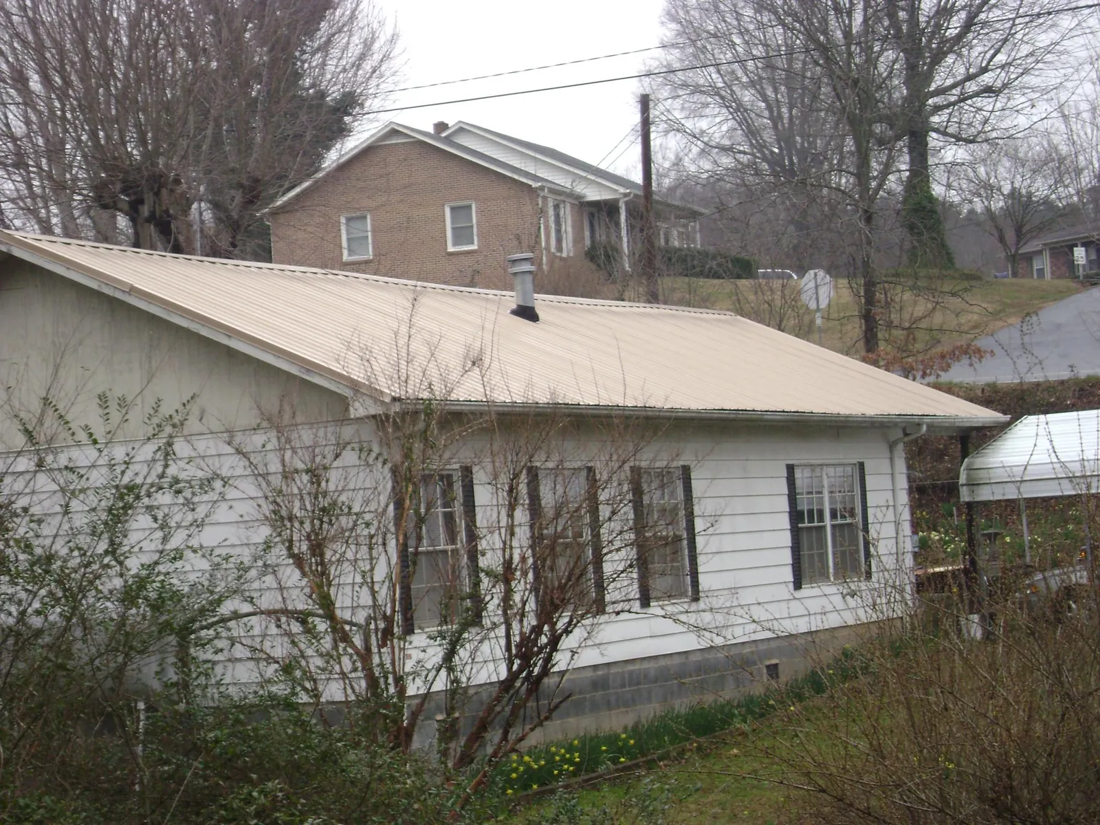 Tan metal roof on a white sided house set into a hillside — Commercial Roofing by Roofing Brothers in Gibbonsville